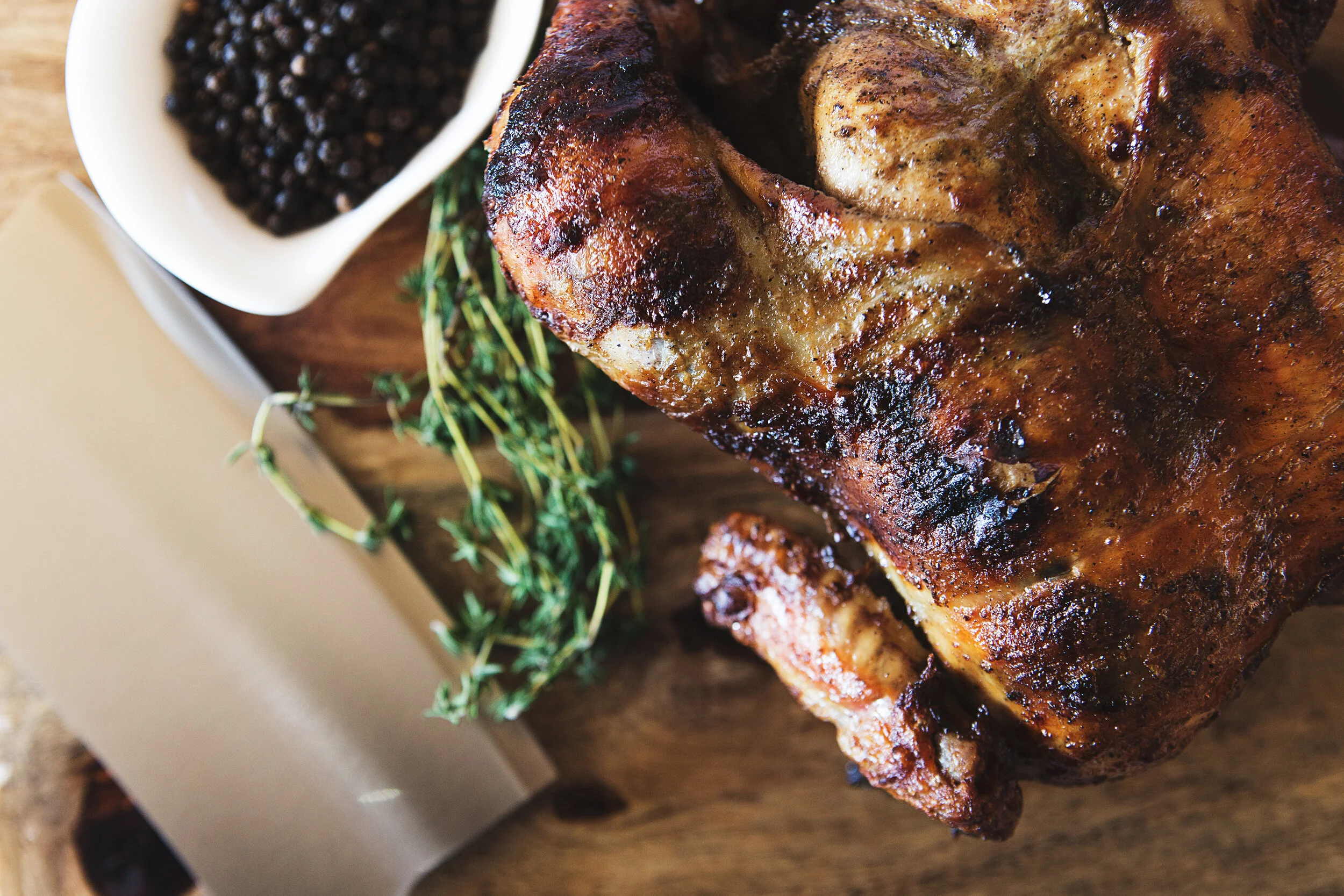 Charcoal-broiled Peruvian rotisserie chicken on a wooden board with fresh thyme and peppercorns
